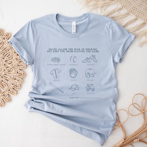 Peut inclure: T-shirt bleu clair avec un motif sur le th&egrave;me du baseball. Le motif comprend le texte "NEVER ALLOW THE FEAR OF STRIKING OUT KEEP YOU FROM PLAYING THE GAME" et des illustrations d'&eacute;quipements de baseball, notamment une batte, une balle, un gant, des crampons, un casque et une casquette.