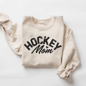 May include: A beige sweatshirt with the text "HOCKEY MOM" printed in black on the front.