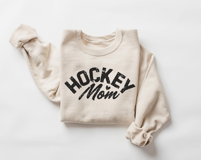 May include: A beige sweatshirt with the text "HOCKEY MOM" printed in black on the front.