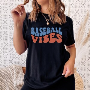 May include: A black t-shirt with the text "BASEBALL VIBES" in a retro, colorful font.
