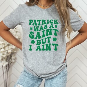 May include: A gray t-shirt with a green graphic that reads "Patrick was a* Saint *but* I ain't".