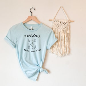 May include: A light blue t-shirt with a black graphic of a dog and the text "Pavlov? That rings a bell."