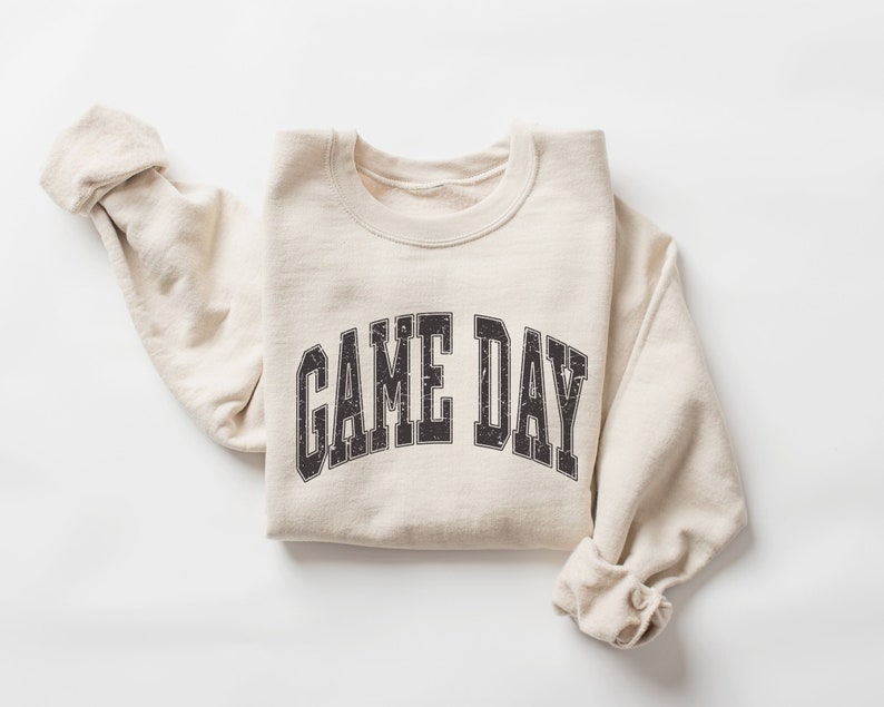 May include: A beige sweatshirt with the text "GAME DAY" printed in black on the front.