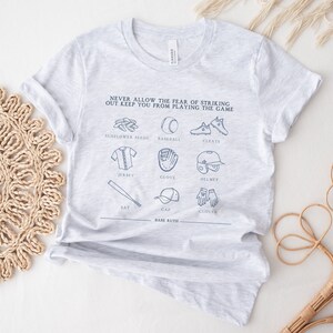 Peut inclure: T-shirt gris avec un th&egrave;me de baseball. Le texte dit "Ne laissez jamais la peur de frapper un home run vous emp&ecirc;cher de jouer au jeu." Le t-shirt pr&eacute;sente des illustrations d'&eacute;quipements de baseball, notamment une batte, un gant, une casquette, des graines de tournesol, des crampons, un maillot et un casque.