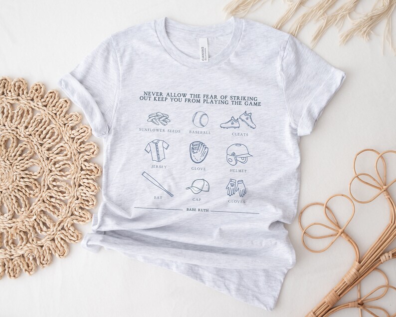 Peut inclure: T-shirt gris avec un th&egrave;me de baseball. Le texte dit "Ne laissez jamais la peur de frapper un home run vous emp&ecirc;cher de jouer au jeu." Le t-shirt pr&eacute;sente des illustrations d'&eacute;quipements de baseball, notamment une batte, un gant, une casquette, des graines de tournesol, des crampons, un maillot et un casque.