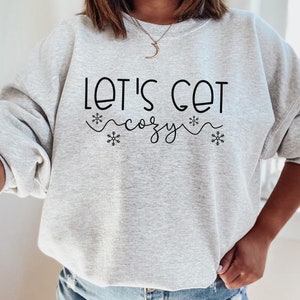 May include: A gray sweatshirt with the text "Let's Get Cozy" in black lettering with snowflake accents.