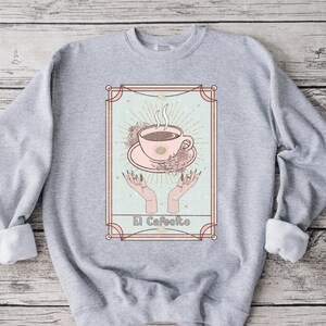 May include: A gray sweatshirt with a graphic print of a coffee cup in a vintage style frame. The text "El Cafeito" is printed below the cup.