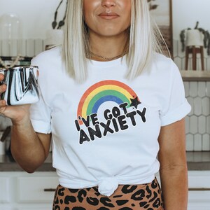 May include: White t-shirt with a rainbow and the text "I've got anxiety" in black lettering.