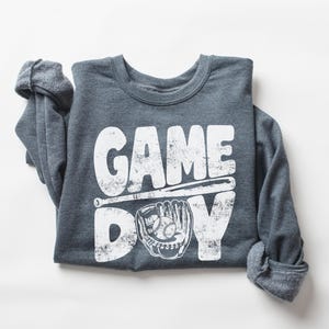 May include: A gray long-sleeve shirt with a white distressed graphic that says "GAME DAY" with a baseball bat and glove.