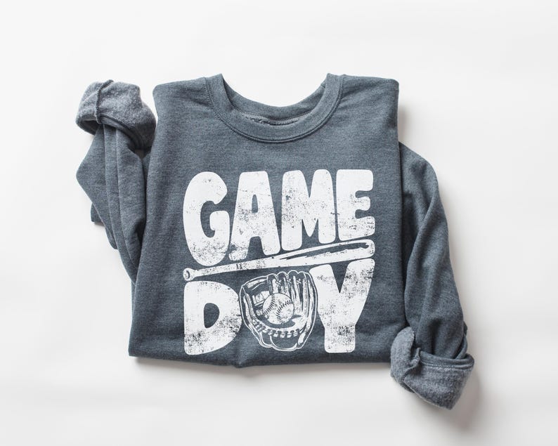 May include: A gray long-sleeve shirt with a white distressed graphic that says "GAME DAY" with a baseball bat and glove.