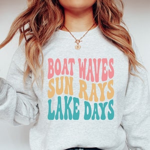 May include: A gray sweatshirt with the text "Boat Waves Sun Rays Lake Days" in a retro font with pink, yellow, and blue colors.