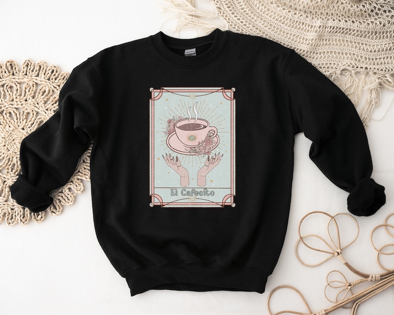 May include: Black sweatshirt with a graphic of a coffee cup with steam rising from it, surrounded by flowers and hands. The text "El Cafeito" is below the cup.