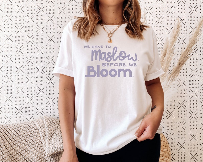 May include: White t-shirt with the text "We have to Maslow before we Bloom." printed in purple.