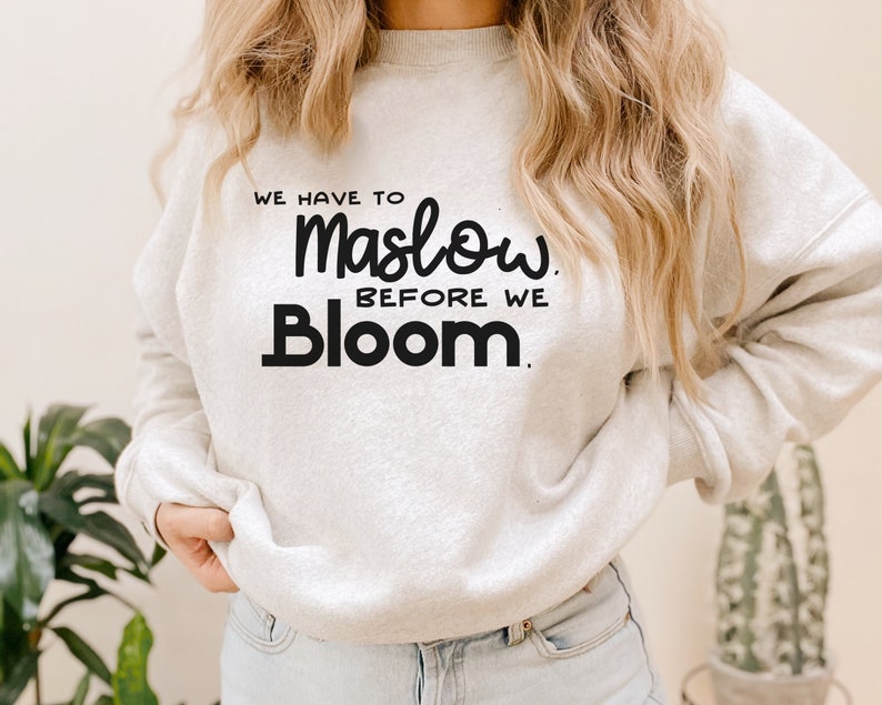 May include: A white sweatshirt with the text "We have to Maslow before we Bloom." printed in black.