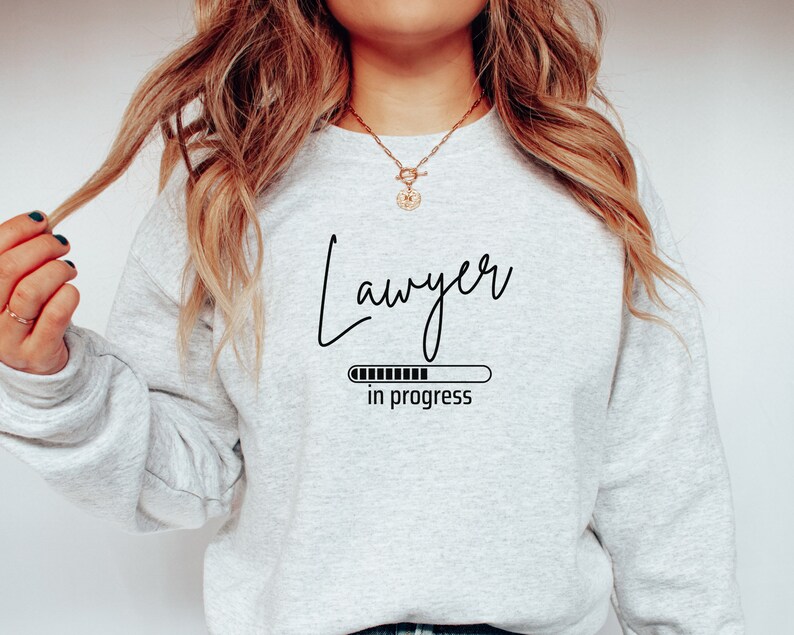 Op de afbeelding: Grijs sweatshirt met de tekst "Advocaat in uitvoering" en een voortgangsbalkgrafiek.