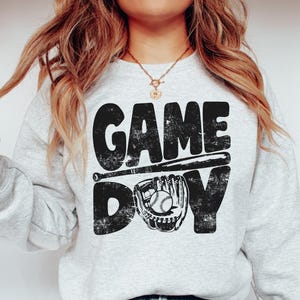 May include: A gray sweatshirt with the text "GAME DAY" in black with a baseball bat and glove graphic.