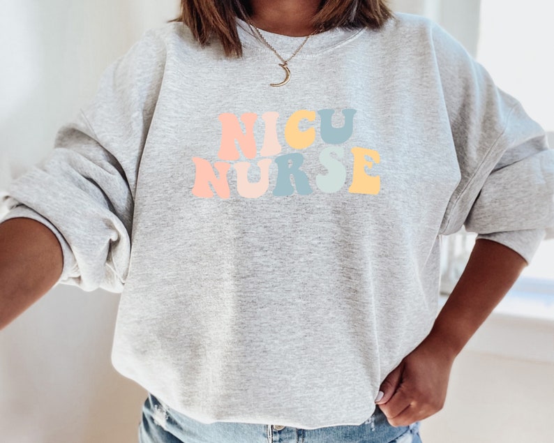May include: A grey sweatshirt with the words "NICU NURSE" in rainbow colours.