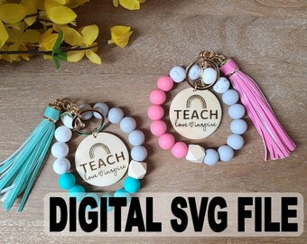 May include: Two beaded keychains with wooden round charms. The charms have a rainbow design and the words "TEACH love inspire". One keychain has a pink tassel, the other has a teal tassel. The keychains are surrounded by light blue, white, and pink beads.