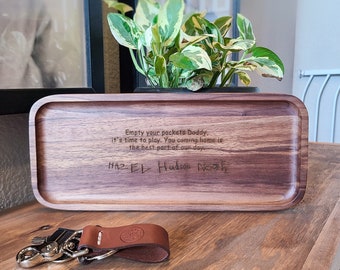 May include: A rectangular wooden valet tray with rounded corners featuring the engraved text: Empty your pockets Daddy, it's time to play. You coming home is the best part of our day. Below the text are the names Hazel, Hudson, and Noah.