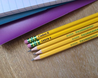 May include: Three yellow wooden pencils with pink erasers and green metal ferrules. Two pencils are personalized with the name Caden R in black text. All pencils feature the green printed text DIXON TICONDEROGA and have sharpened graphite tips.