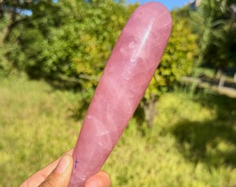 Könnte beinhalten: Ein polierter, zylindrischer Rosenquarz-Kristallstab mit einer glatten, abgerundeten Spitze und einer verjüngten Basis. Der Stein weist einen durchscheinenden, blassrosa Farbton mit sichtbaren inneren Rissen und natürlichen Adern auf.