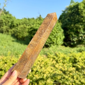 May include: A tall, hexagonal crystal point with a polished surface, featuring a golden-brown colour with intricate, fibrous, and needle-like inclusions throughout the stone, displaying a natural chatoyant lustre across its elongated structure.