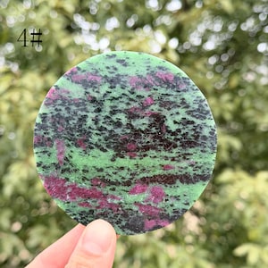 Könnte beinhalten: Ein runder, polierter Stein mit einem gesprenkelten Muster aus Grün, Schwarz und Kastanienbraun. Der Stein wird in einer Hand gehalten und die Nummer "4#" ist in der oberen linken Ecke sichtbar. Die Oberfläche des Steins hat ein gesprenkeltes Aussehen.