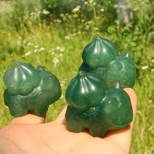 May include: Three small, translucent green stone carvings shaped like creatures with bulbous, rounded structures on their backs. Each figure features a smooth, polished surface with subtle variations in the deep green mineral coloration.