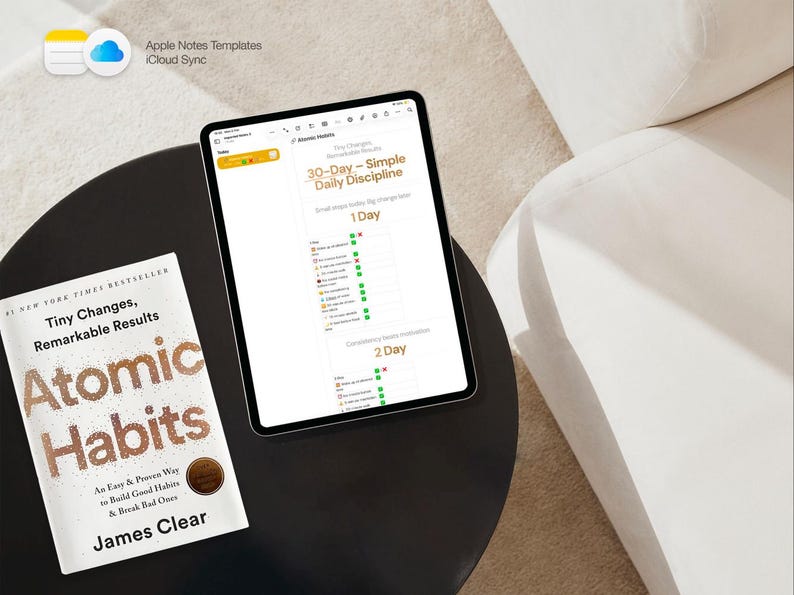 May include: A tablet displaying a 30-Day Daily Discipline chart sits on a black table next to a copy of "Atomic Habits" by James Clear. The book cover features gold lettering. The tablet's screen shows a habit tracker. The image is taken from above.