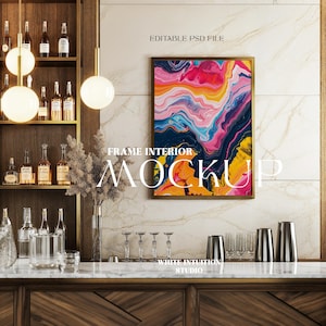 May include: A framed abstract painting with colorful swirls of pink, yellow, blue, and purple against a dark blue background. The frame is gold and the painting is hanging on a white marble wall above a bar counter.