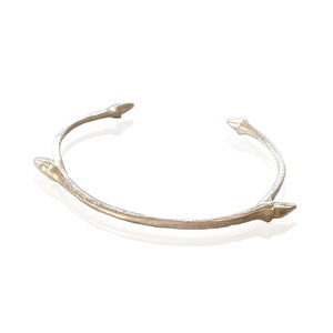 May include: A silver bangle bracelet with a twig-like design and pointed ends.