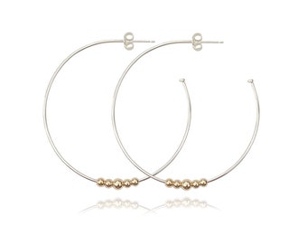 May include: Silver hoop earrings with a row of gold beads.