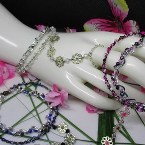 May include: Four silver bracelets with different colored beads and charms. The bracelets are on a white mannequin hand. The bracelets have silver chain links, silver flowers, and pink, blue, and black beads.