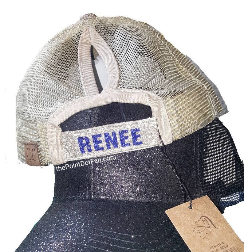Pode incluir: Um bon&eacute; de beisebol preto com glitter, parte traseira em rede bege e abertura para rabo de cavalo alto. A tira traseira apresenta o nome RENEE em letras azuis brilhantes. Uma pequena etiqueta castanha est&aacute; presa ao lado, log&oacute;tipo C.C. vis&iacute;vel.