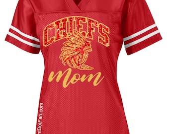 May include: Red football jersey with white stripes on the sleeves. The jersey features the word "CHIEFS" in a glittery design above a Native American headdress graphic. The word "Mom" is written in gold script below the graphic. The website address thePointDotFan.com is printed on the side.