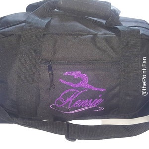 May include: Black gym bag with a purple glitter design of a gymnast and the name "Kenzie". The bag has a zippered pocket on the front and the text "@thePointFan" on the side.