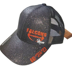 May include: Black glitter baseball cap with a mesh back. The cap features the text "Falcons Mom" in orange and white, along with "GO! 316'23" in orange. The website "thePointDotFan.com" is printed on the side.