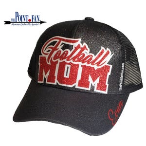 Pode incluir: Um bon&eacute; trucker preto com glitter e o texto Football MOM em glitter vermelho no painel frontal. O nome Evan aparece em glitter vermelho na aba. O texto thePointDotFan.com est&aacute; impresso verticalmente no painel lateral do bon&eacute;.