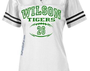 May include: White jersey with black and white stripes on the sleeves. The jersey has a green football graphic with the text "WILSON TIGERS 26" on the front.