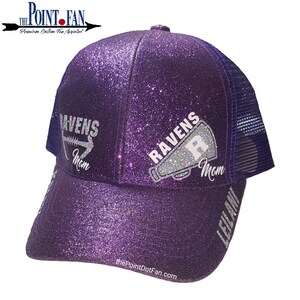 May include: A purple glitter trucker hat with a mesh back. The hat features the text "RAVENS Mom" in silver glitter, along with a football and a megaphone graphic. The name "LEILANI" is printed on the brim. The Point Fan logo is visible.