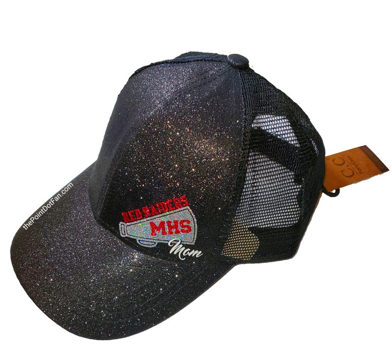 May include: Black glitter trucker hat with a mesh back. The front of the hat features the text "REARADERS MHS Mom" in red and white. The hat has a curved brim and a small button on top. The website "ThePointDotFan.com" is printed on the side.