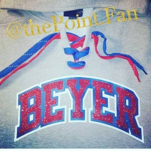 May include: A gray hoodie with red and blue laces. The hoodie has a red and blue glitter design that says "BEYER" on the front.