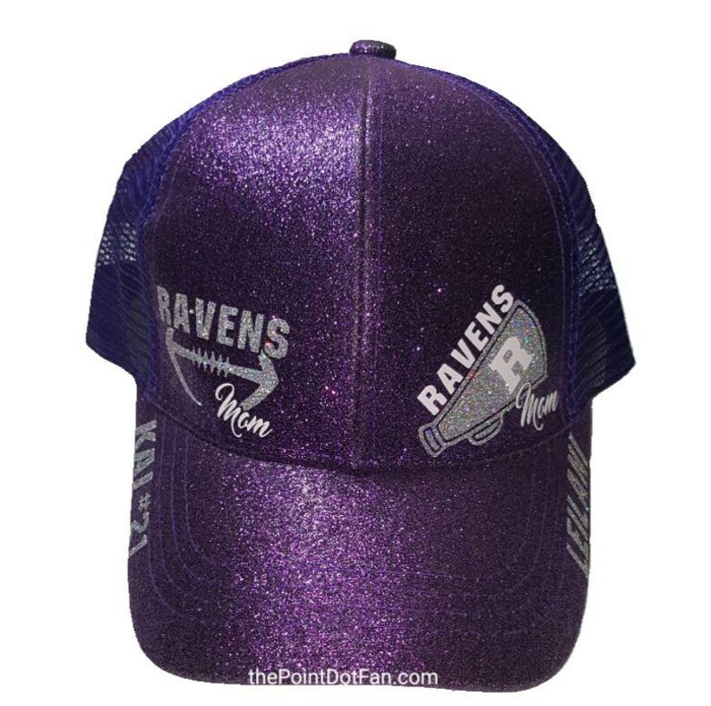 Pu&ograve; includere: Cappellino da camionista viola con paillettes con un designo di paillettes argentate di un pallone da calcio e le parole "Ravens Mom" su un lato e un megafono con le parole "Ravens Mom" sull'altro lato.
