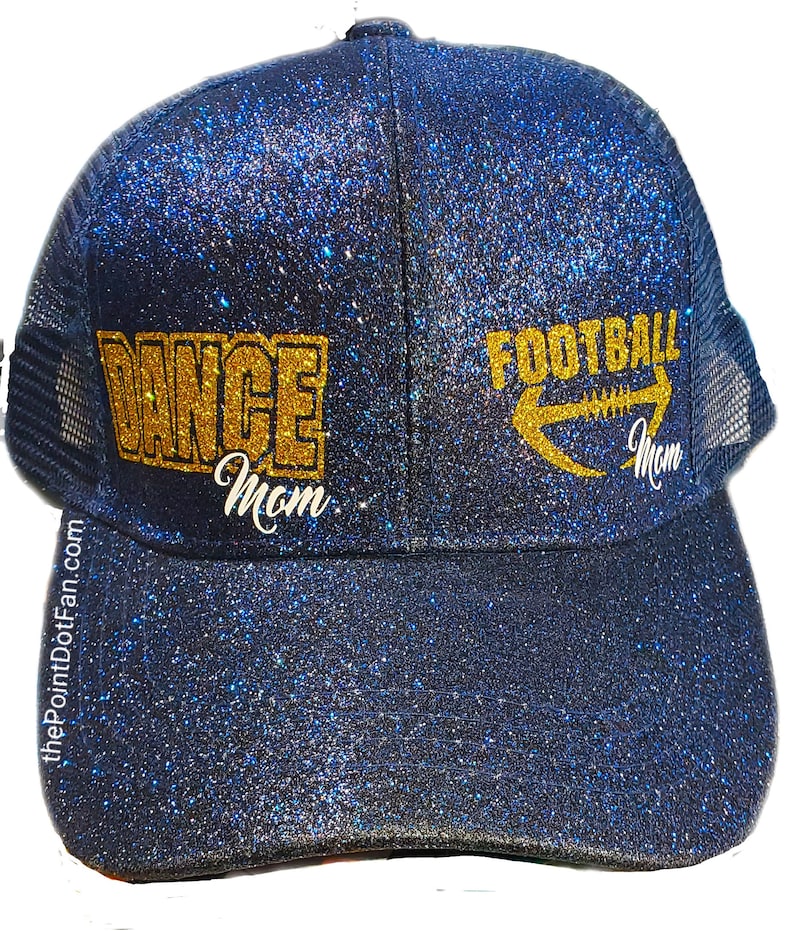 May include: A navy blue glitter trucker hat with the words "DANCE Mom" and "FOOTBALL Mom" in gold lettering. The hat has a mesh back and a curved brim. The website address thePointDotFan.com is printed on the side of the hat.