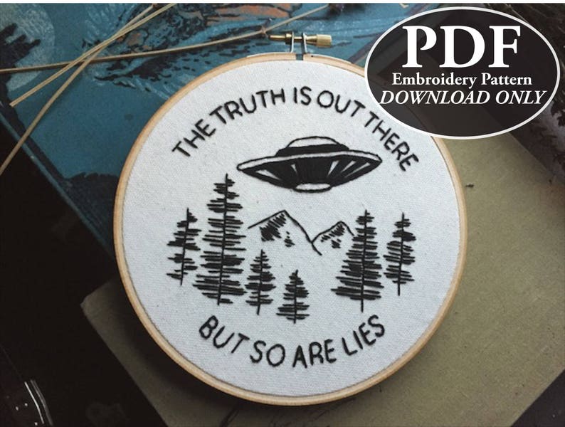 May include: A white embroidery hoop with a black and white design. The design features a UFO, mountains, and trees, with the text "THE TRUTH IS OUT THERE BUT SO ARE LIES". A PDF embroidery pattern download is available.