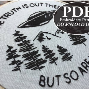 May include: Embroidered hoop art featuring a black UFO, trees, and mountains. The text reads "THE TRUTH IS OUT THERE BUT SO ARE LIES." A PDF embroidery pattern download is available.