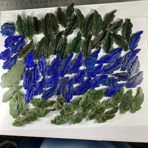 Puede incluir: Una colección de colgantes en forma de hoja de piedras preciosas verdes y azules. Las hojas están talladas en jade y lapislázuli.