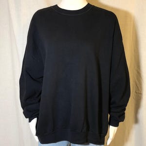 Puede incluir: Una sudadera negra lisa con cuello redondo. La parte superior de manga larga tiene un ajuste relajado y se muestra en un maniquí. La sudadera está hecha de un material suave y es adecuada para ropa casual.