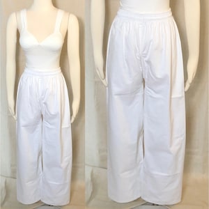 May include: White, wide-leg pants with an elastic waistband. The pants are shown on a mannequin, paired with a white top. The fabric appears to be lightweight and suitable for warm weather. The pants have a relaxed fit.