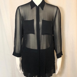 May include: A black long-sleeved button-down shirt made of a sheer, translucent fabric. The shirt features a classic collar, a front button placket, and two square chest pockets. The sleeves are finished with solid black cuffs at the wrists.